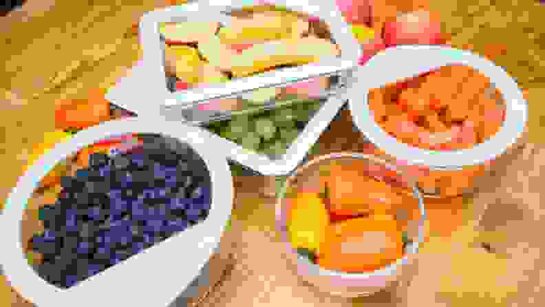 A table with glass Pyrex containers filled with fresh fruits and veggies.