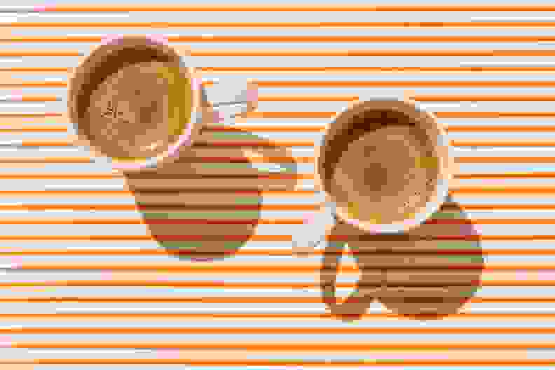 Two cups of coffee sitting on an orange and white striped tablecloth