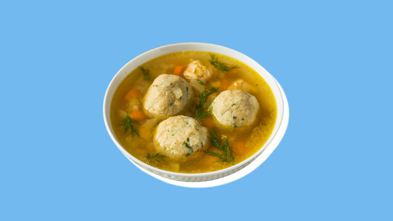 A small bowl of matzo ball soup with small vegetables inside.