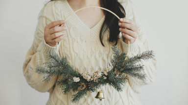 A person in a cream sweater holding a hoop wreath in their hands.