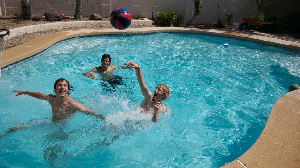 Three youths play pool basketball in an in-ground swimming pool.