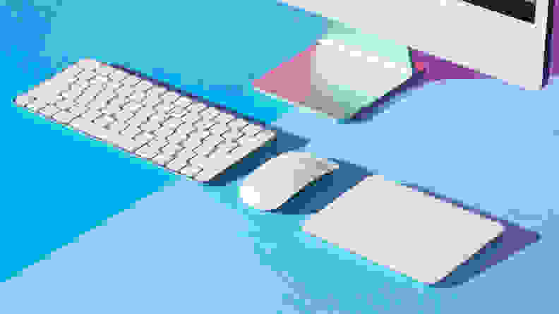 Desktop computer peripherals (keyboard, mouse, trackpad) on a blue surface.