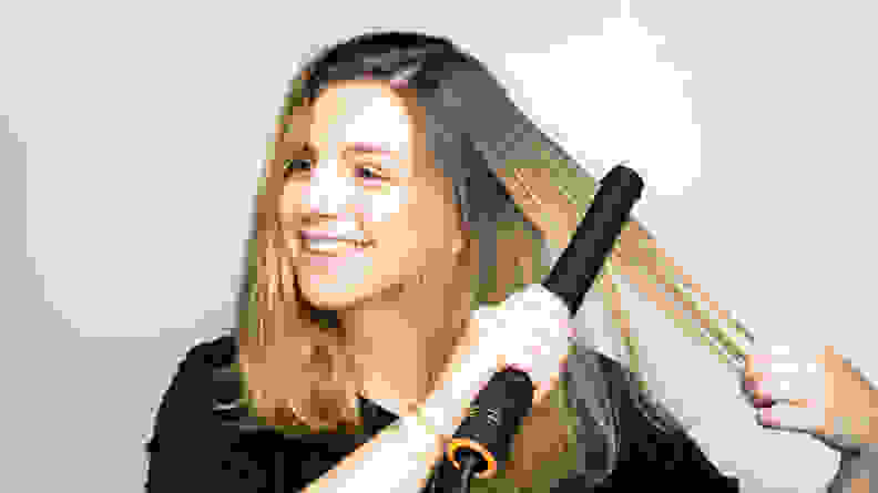 A woman using a hair straightener on her long hair.