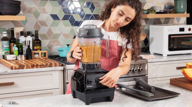 Person using a Vitamix blender to process ingredients for butternut squash soup.