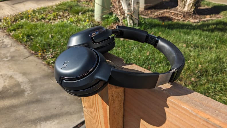 The JBL Tour One M2 headphones sitting on top of a wooden post on a sunny day.