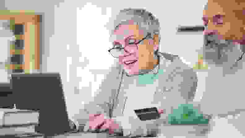 Two elderly people shopping on a laptop with a credit card.