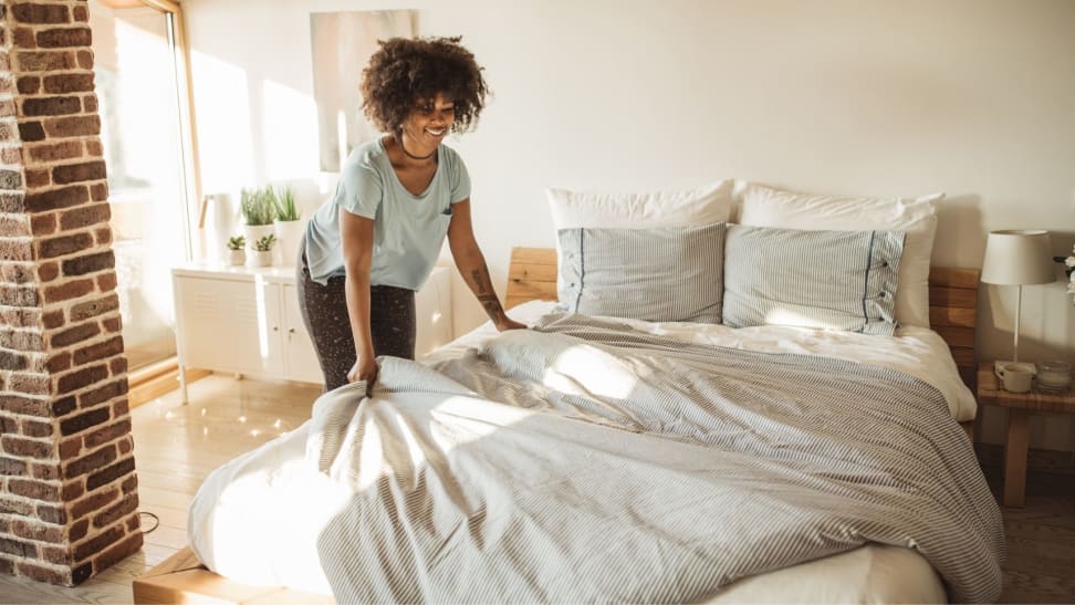 A person positions a duvet cover over a mattress in a bedroom