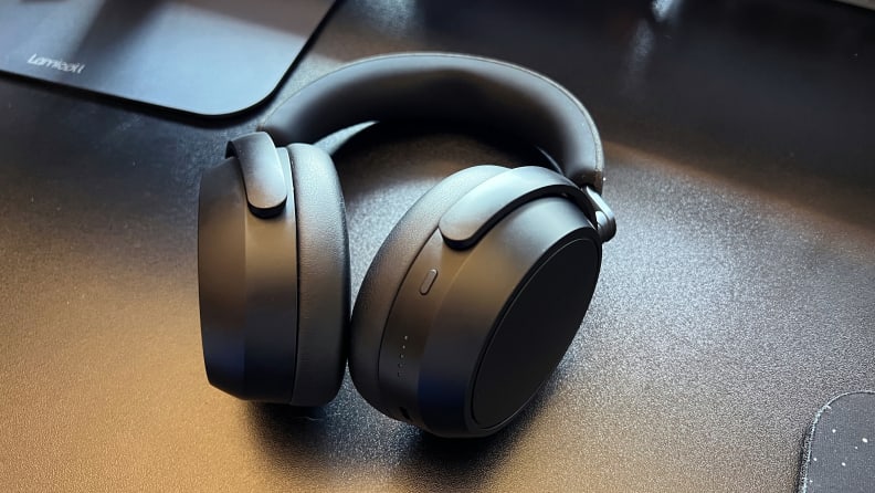 A pair of black headphones sits on a black desk with gear behind.