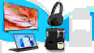 A TV displaying a red leaf with beads, a pair of Sony headphones, a white washing machine, a black Keurig coffee maker, and a Samsung convertible laptop displaying the Windows 11 Start Menu against a light blue, dark blue, and beige background.