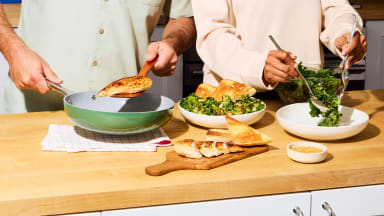Two people prepare a fresh salad and toasted bread in a bright kitchen, showcasing delicious home cooking inspired by a HelloFresh promo.