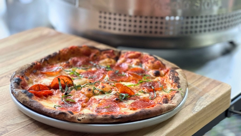 Small pepperoni pizza in dish on wooden cutting board.