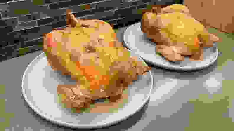 Two roasted whole chickens on top of plates on countertop.