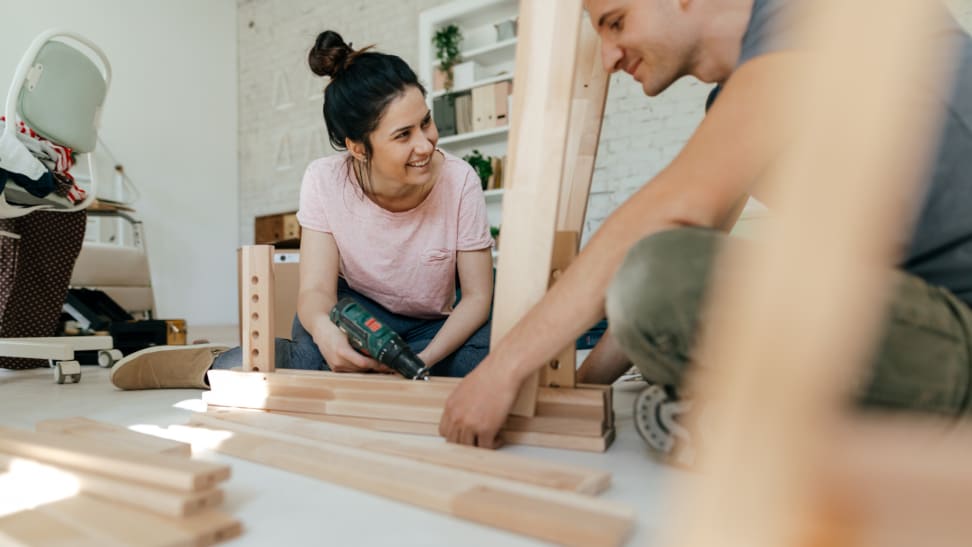 Couple assembling furniture together on floor while smiling.