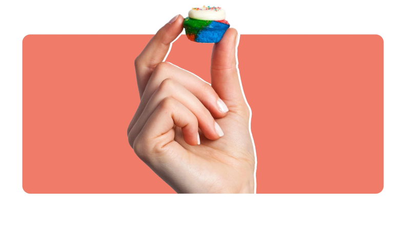 Person holding a small, colorful Baked by Melissa mini cupcake in their fingers.