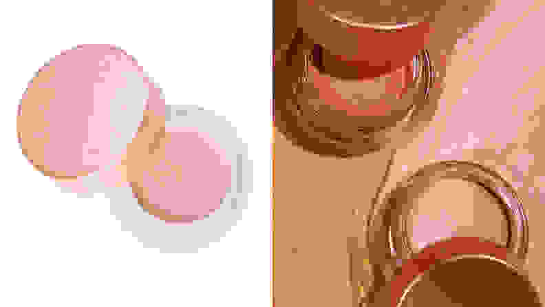 On the left: On a white background sits the Becca Cosmetics Under Eye Brightening Corrector. The bottom of the jar is clear and the rose gold top is off to the side to reveal a light peach-toned concealer inside. On the right: The Becca Cosmetics Under Eye Brightening Corrector in a darker color sits with its cap off on a swatch of the dark concealer. To the right is the lighter, peach colored Becca Cosmetics Under Eye Brightening Corrector on top of a light pink swatch of concealer.