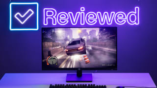 The HP X27q monitor displaying a racing video game with the Reviewed.com logo in neon light behind it.