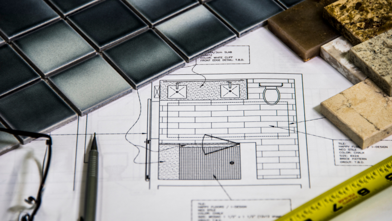 A countertop with a design blueprint, pencils, and tiles.