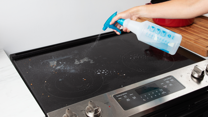 A hand spraying vinegar on a glass stove.