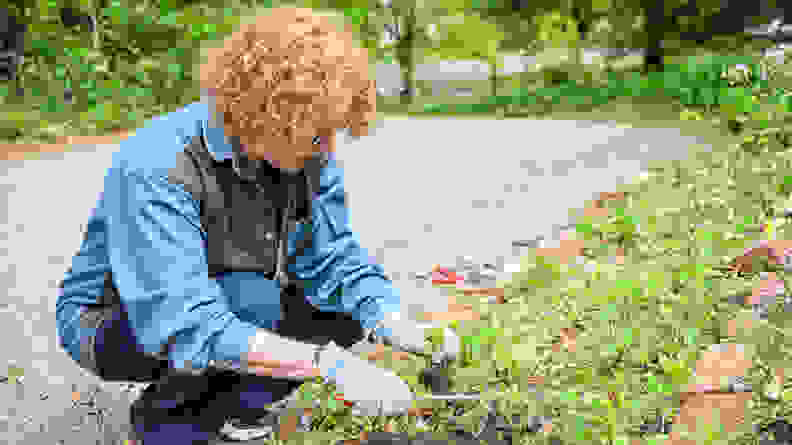 The author, Meg Muckenhoupt, crouching besides a garden to test out a set of gardening gloves.