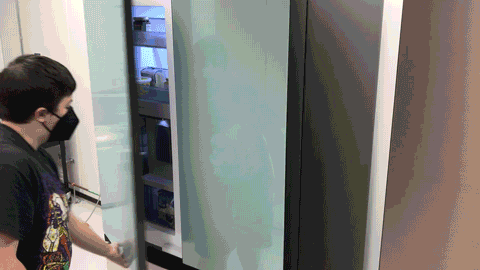 A man is shown opening the door of a Samsung fridge, taking out soda from an inside box and then closing the door.