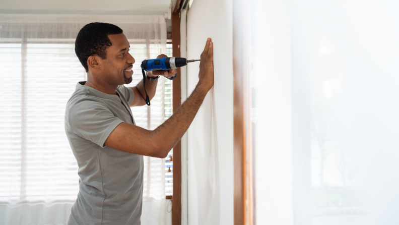 Man smiling while drilling hole into wall with powertool.