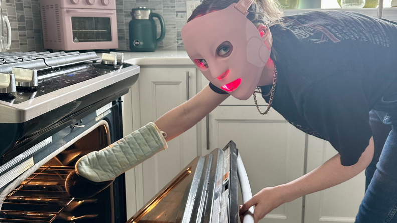 Woman wearing a face mask and pulling something out ofthe oven.