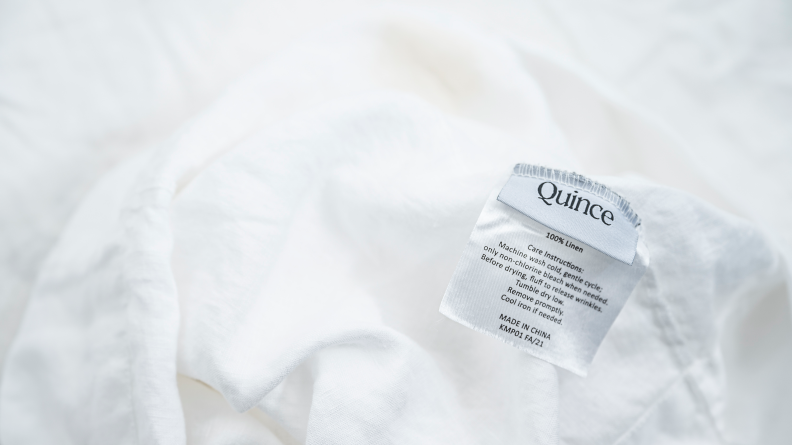 A closeup of the tag on a set of white linen sheets from Quince.
