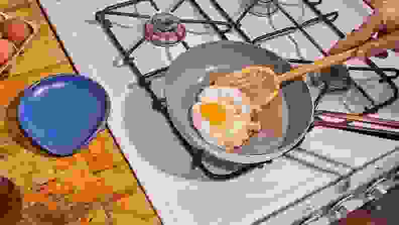 A person flips an egg in a nonstick skillet using a relatively flat wooden spoon.