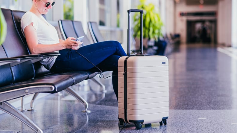 A woman in a chair with Away luggage nearby, among the best 30th birthday gift ideas.