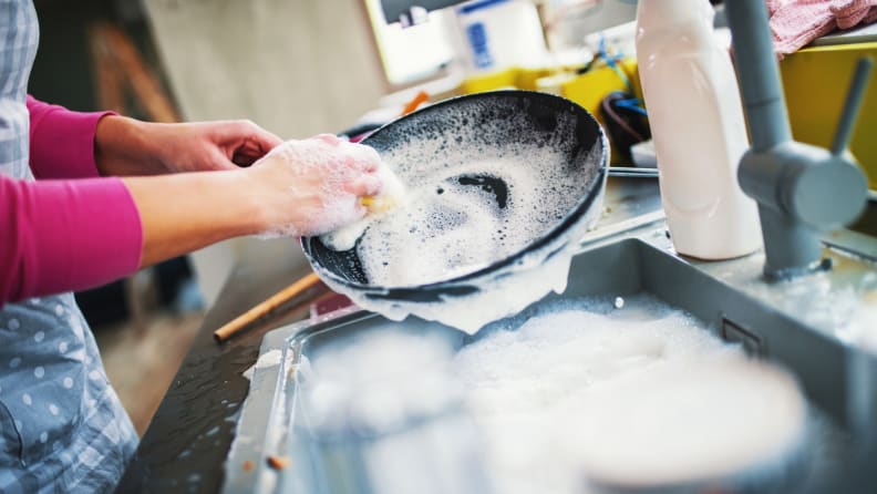 Person washing dishes in kitchen sink.