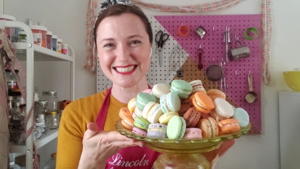 A baker holds a glass plate filled with colorful macarons.