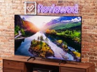 The Hisense U6K displaying a colorful 4K image of a river and a sunset while it sits in front of a brick wall in a living room setting