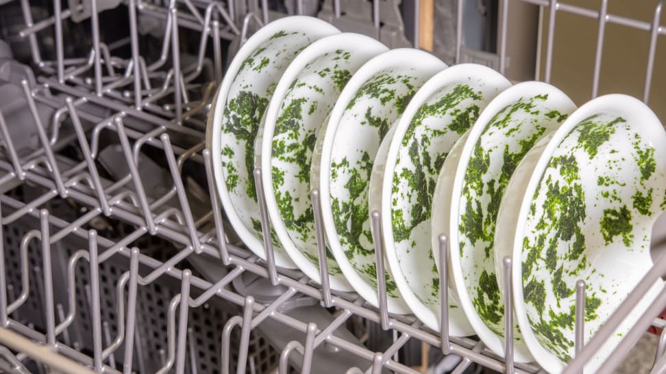 A lot of spinach food waste on a series of bowls in the upper rack of a dishwasher.
