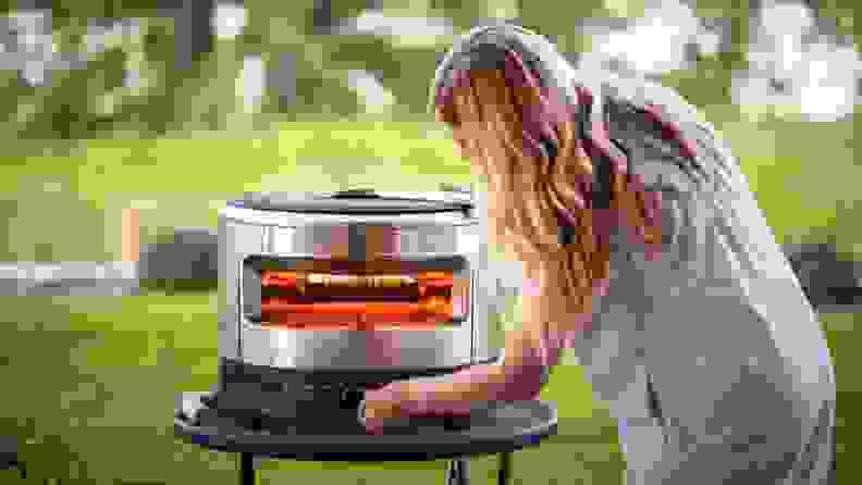 Person crouches down outdoors in front of the Solo Pi Prime to adjust temperature settings with knob.
