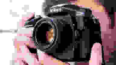 Close-up photo of a person using a Nikon DSLR camera.