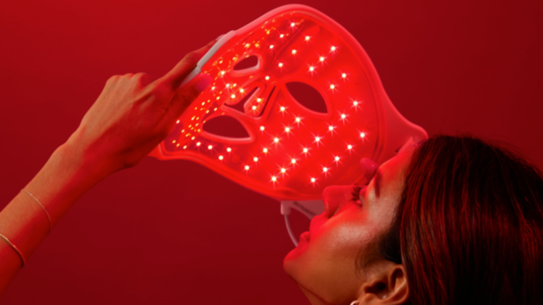 A woman looks at the underside of the illuminated LED mask.