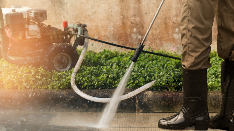 Person using power washer to on driveway and wearing rubber boots