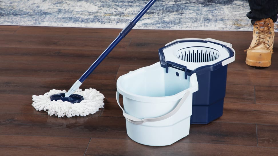 Person using Casabella Clean Water Spin Mop to clean hardwood floor surface next to bucket inside of modern living room setting.