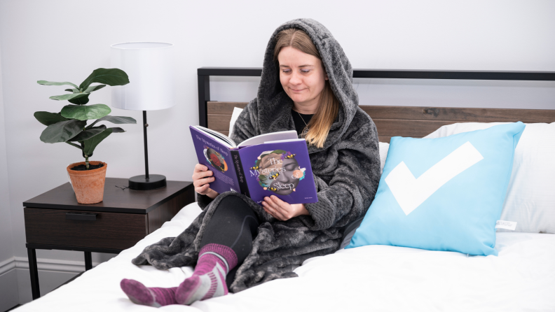 Girl sitting on a bed reading a book.