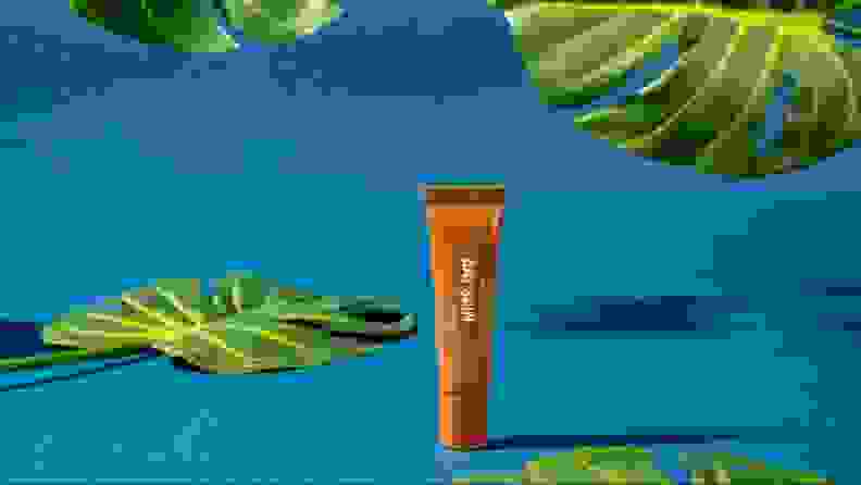 A tube of lip balm against a blue background and foliage.