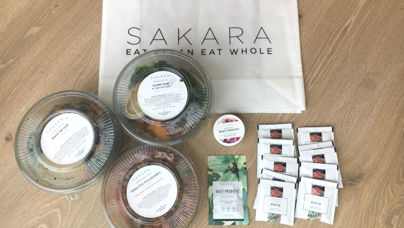 Sakara salads and teas on a wooden countertop with a Sakara bag in the background.