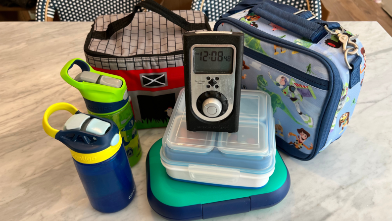 Water bottles, lunch boxes and bento boxes stacked up around a kitchen timer.