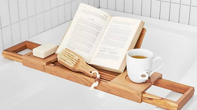 An image of a teakwood bath tray with a book and teacup, all slung over a filled bath.