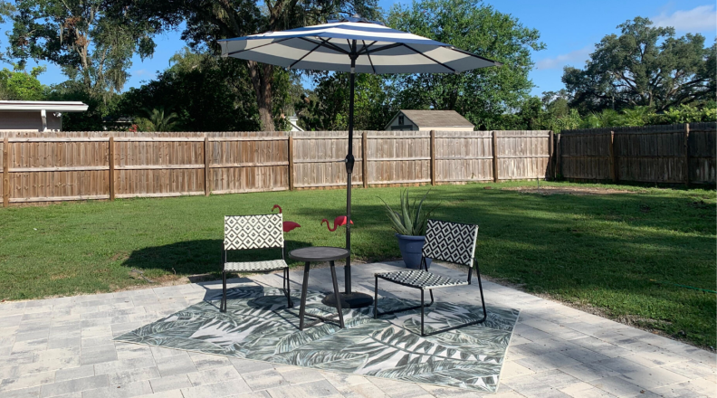 The Ruggable outdoor rug on a backyard patio with two chairs and a patio umbrella