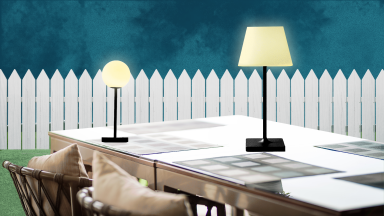 Lamps sitting on an outdoor table in front of a white pickett fence at night.