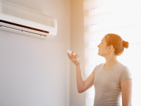 Person using remote to control air conditioner unit mounted on wall.