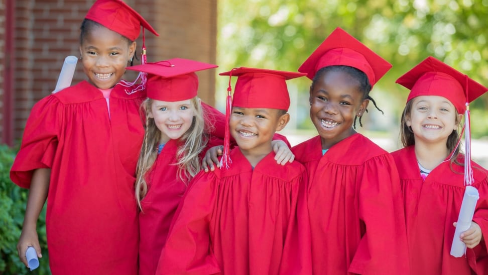 A group of five smiling kindergarten graduates in red grad gowns and caps.