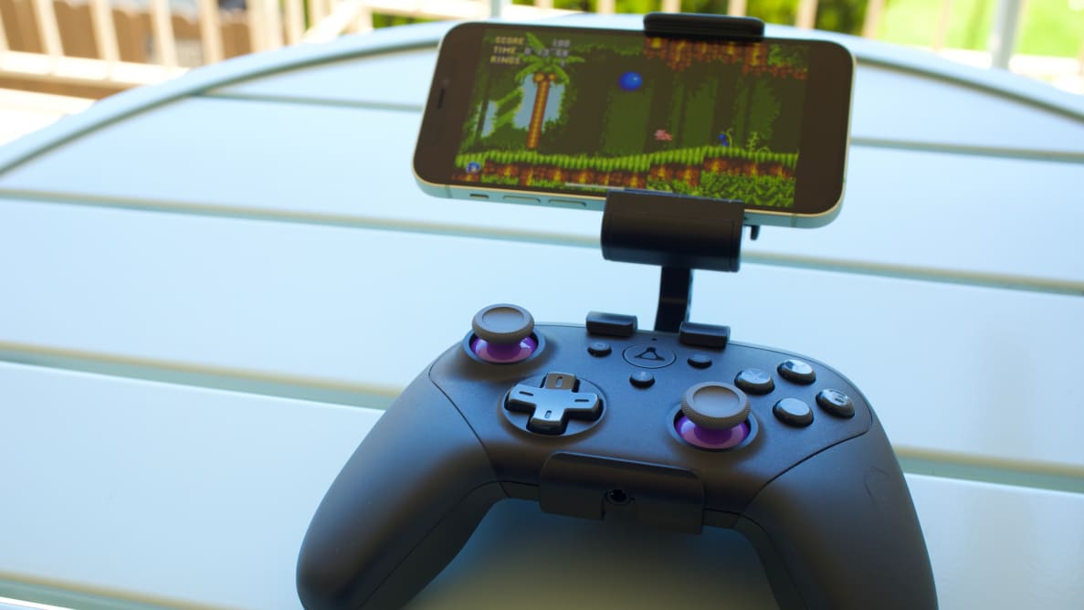 A cell phone attached to a video game controller on top of a white wooden table.