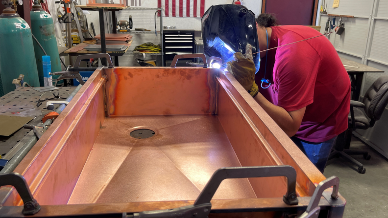Welder using tool to work on copper sink.