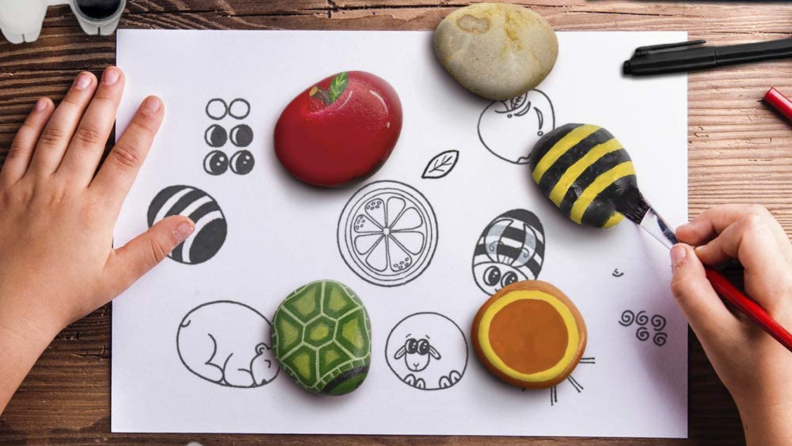 A young child paints rocks.